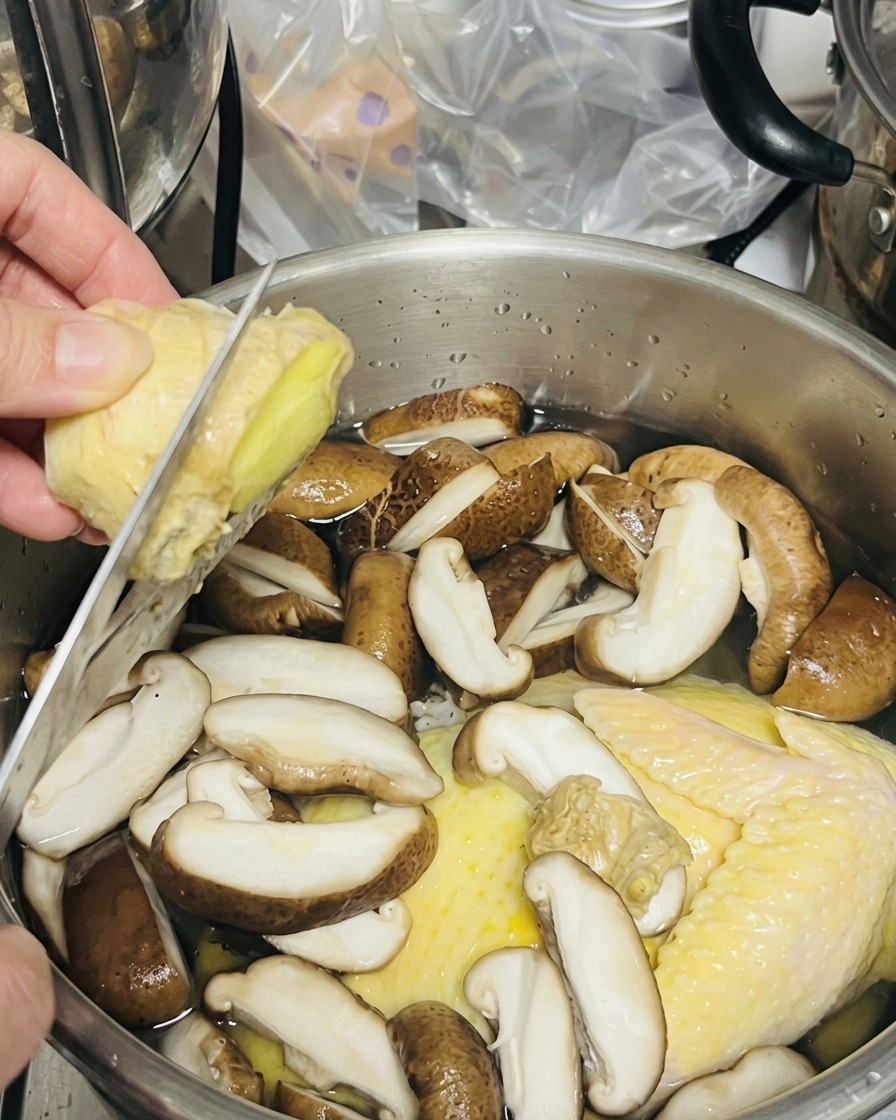 Une personne utilisant un couteau pour trancher du gingembre frais directement au-dessus dune marmite.