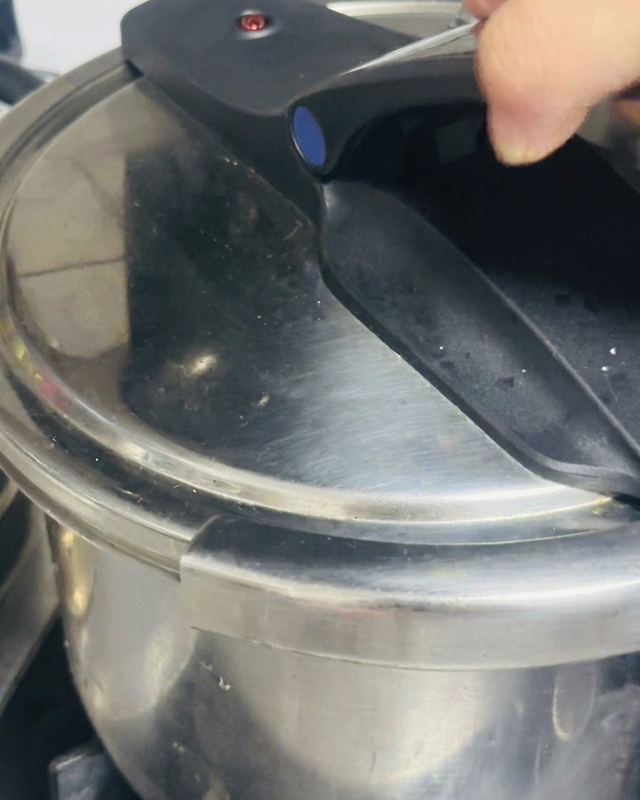 Une main fermant et verrouillant solidement la poignée noire du couvercle dune cocotte-minute en inox.