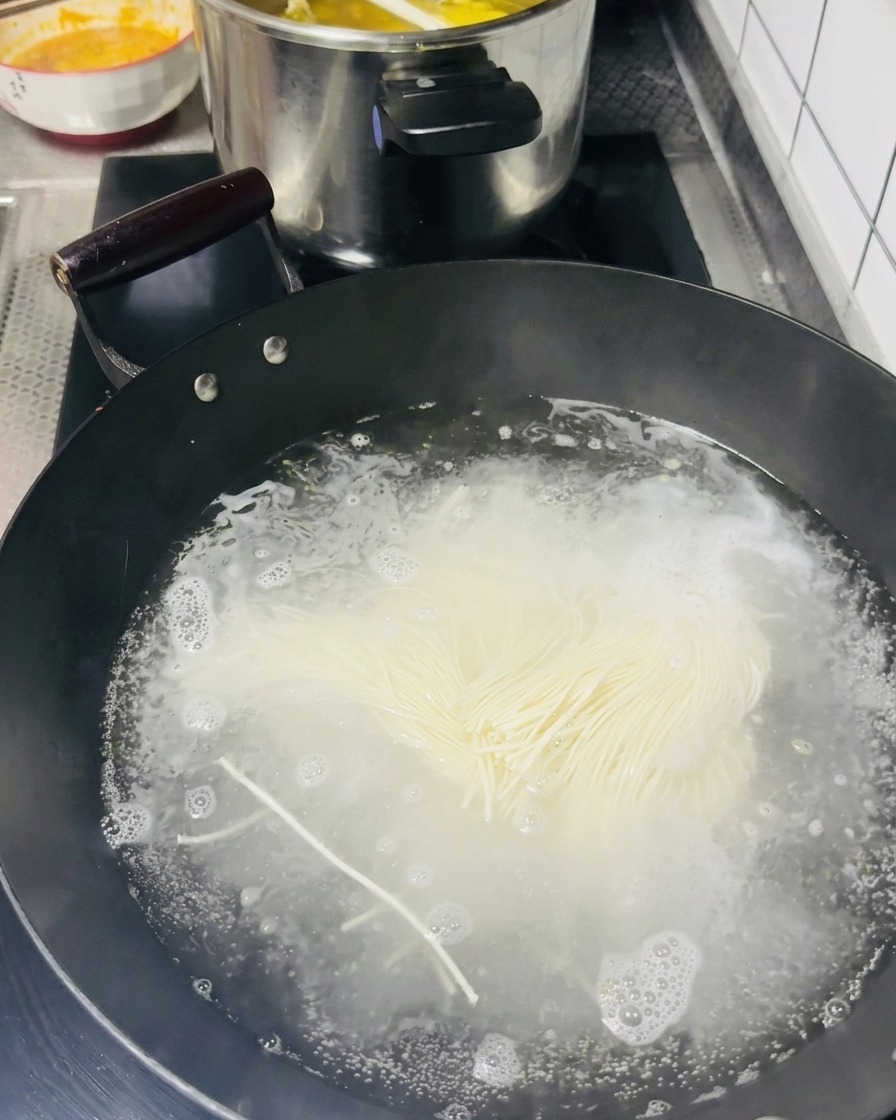 Une botte de nouilles fines crues jetée dans un wok noir rempli deau bouillonnante.