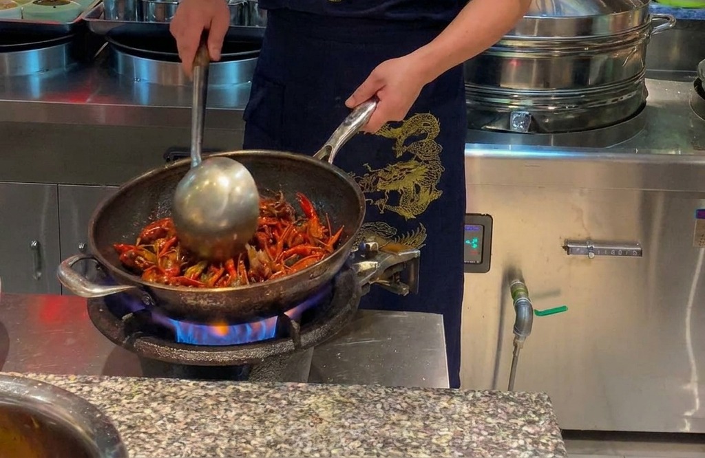 Chef faisant sauter des écrevisses rouges dans un grand wok sur une flamme vive.