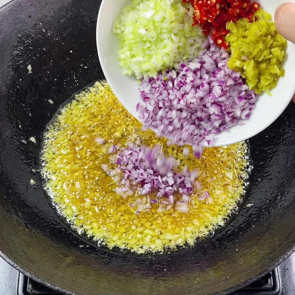 Oignons, ciboule et piments ajoutés à lail dans le wok.