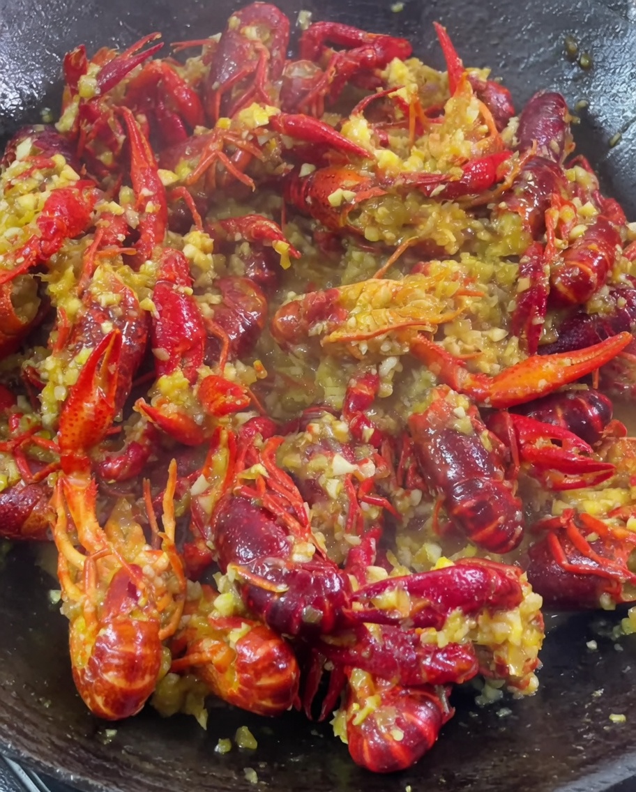 Ail, curry et assaisonnements ajoutés à un wok décrevisses en train de mijoter.