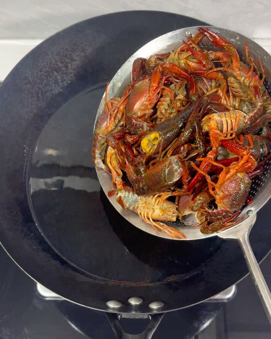 Écrevisses retirées de lhuile chaude dans un wok à laide dune écumoire métallique.