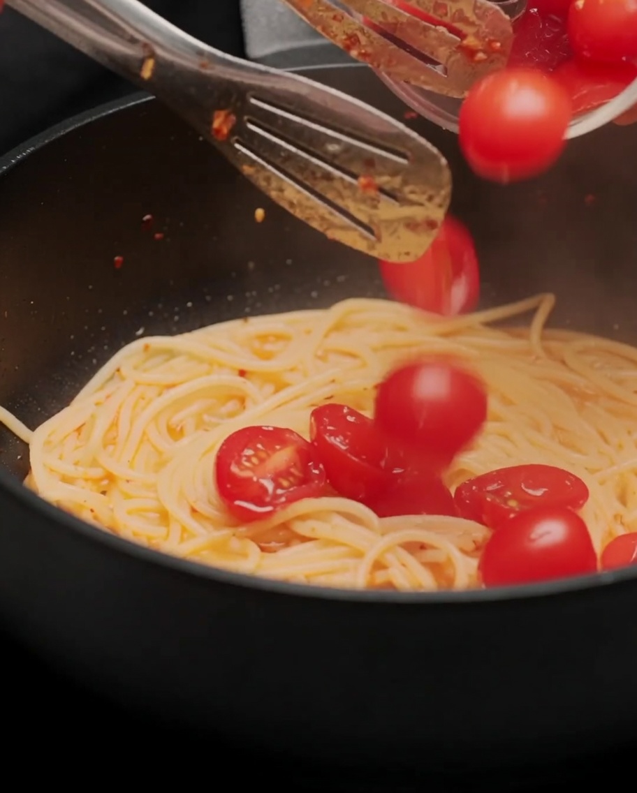 Tomates cerises coupées en deux ajoutées à la poêle de spaghetti et sautées.