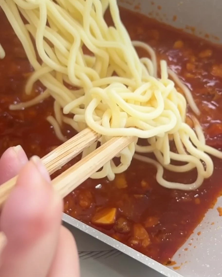 Spaghettis mélangés à la sauce tomate à la viande dans une poêle à laide de baguettes.