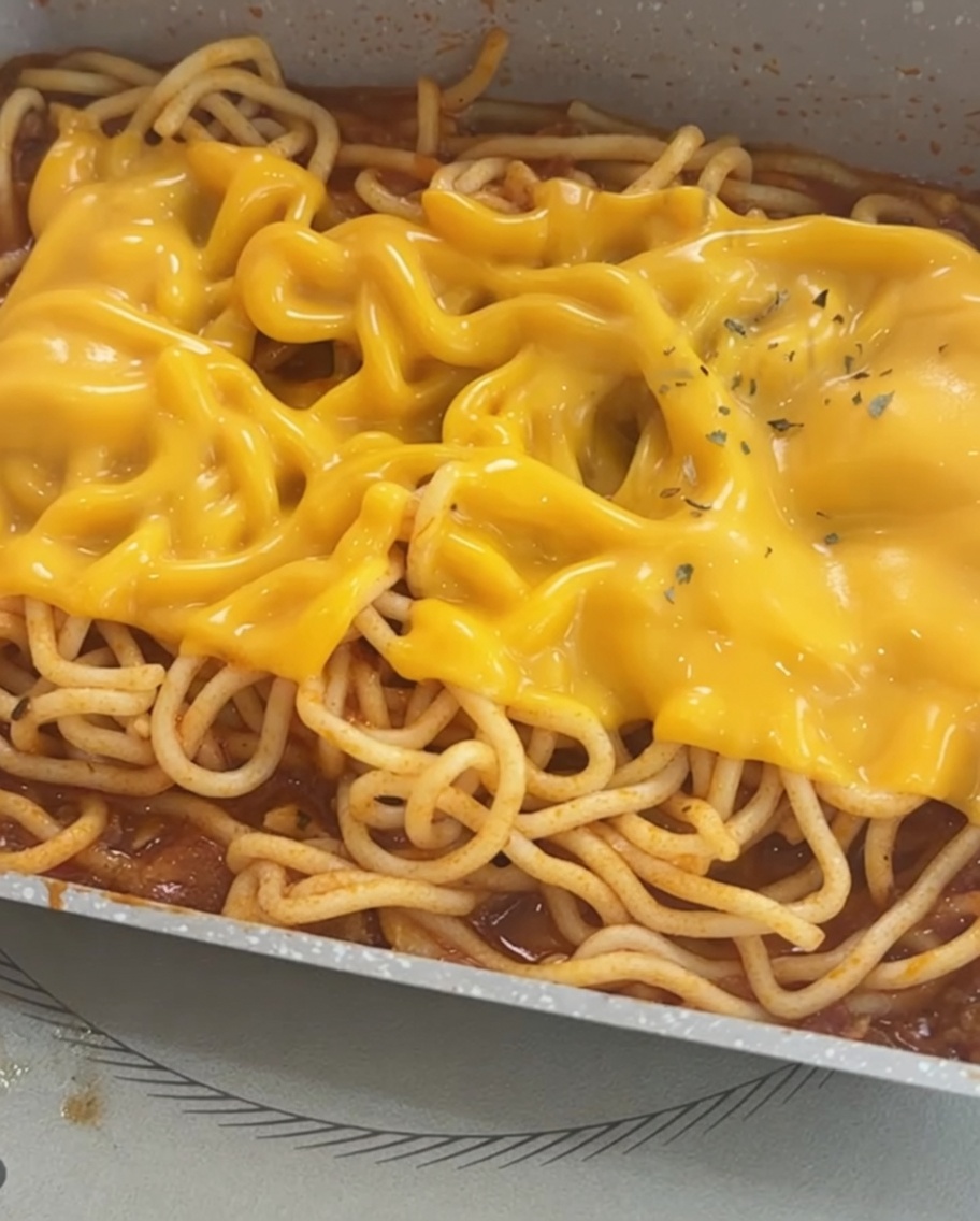 Spaghettis garnis de fromage fondu et parsemés de flocons de persil séché.