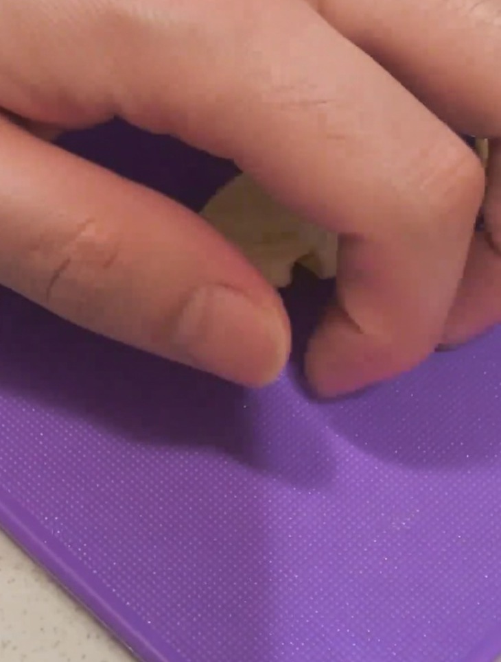 Gros plan dune main écrasant une gousse dail sur une planche à découper avec le plat dun couteau.
