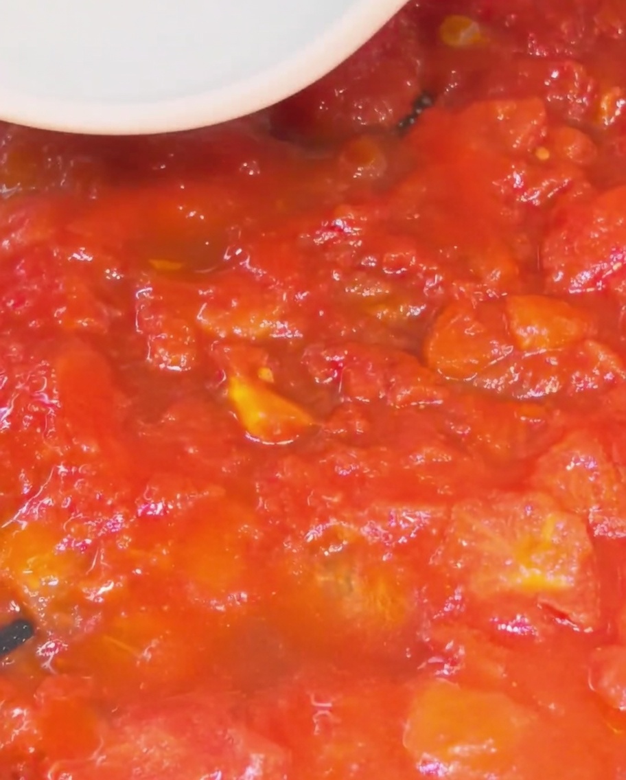 Spatule en silicone écrasant les morceaux de tomate pour former une sauce.