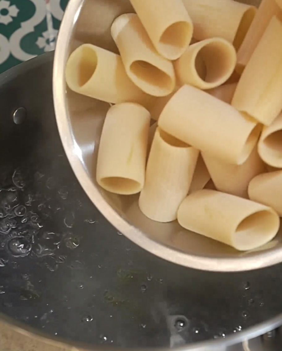 Des rigatoni crus versés dans une casserole deau bouillante.