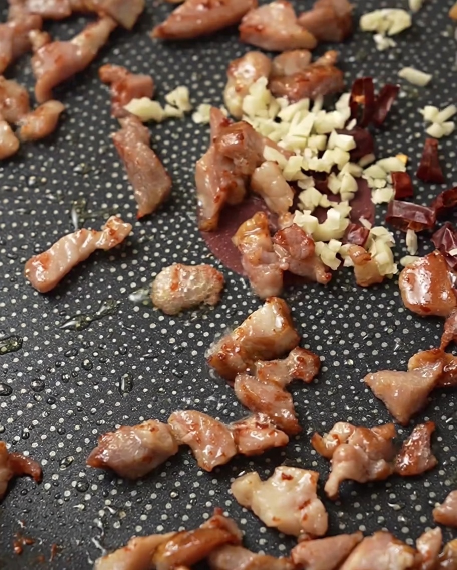 Bacon, ail émincé et piments séchés qui grésillent dans une poêle.
