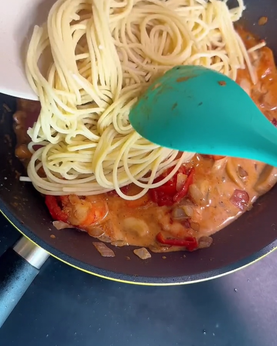 Des spaghettis sont mélangés à la sauce crémeuse dans la poêle avec une spatule.