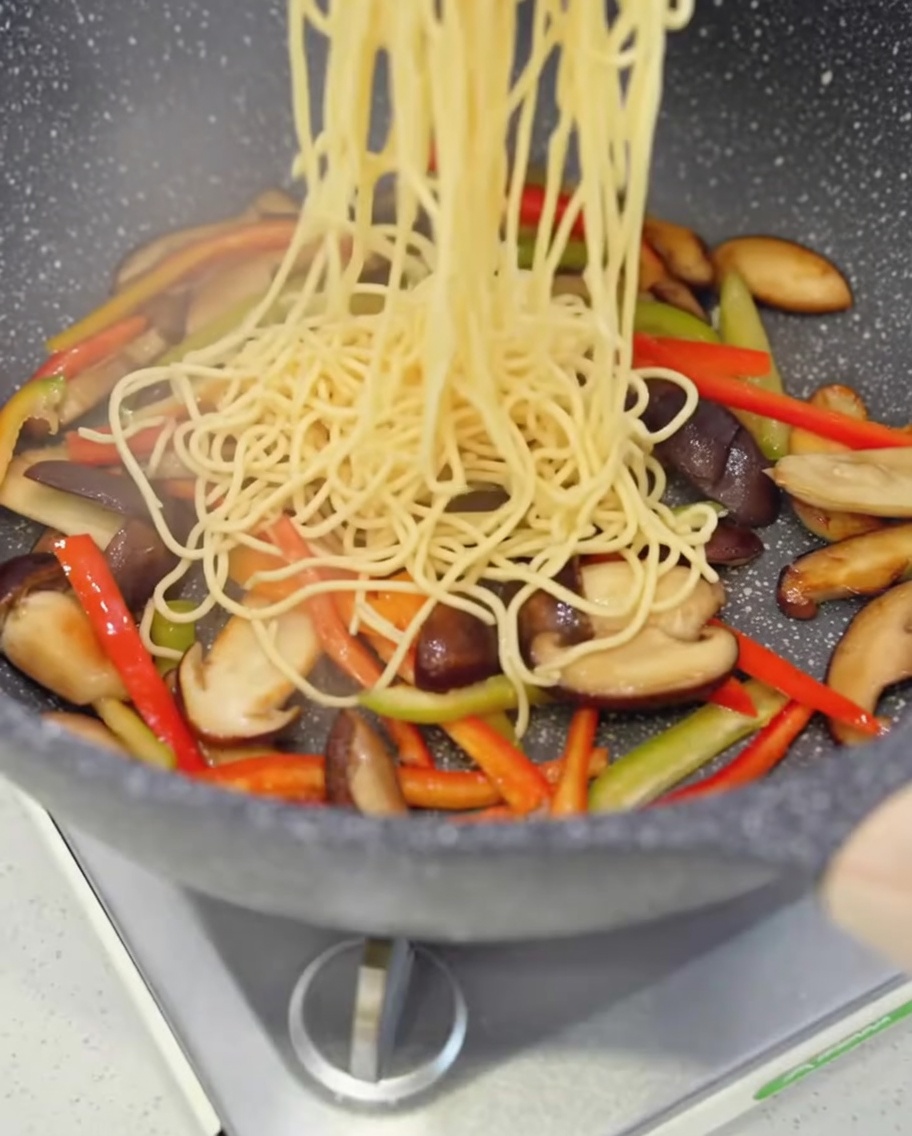 Spaghetti cuits ajoutés dans la poêle avec les champignons et les poivrons.
