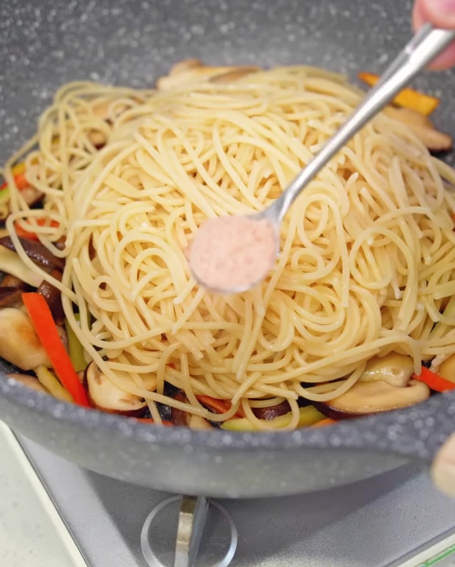 Une petite cuillère de sel saupoudrée sur les spaghetti dans la poêle.