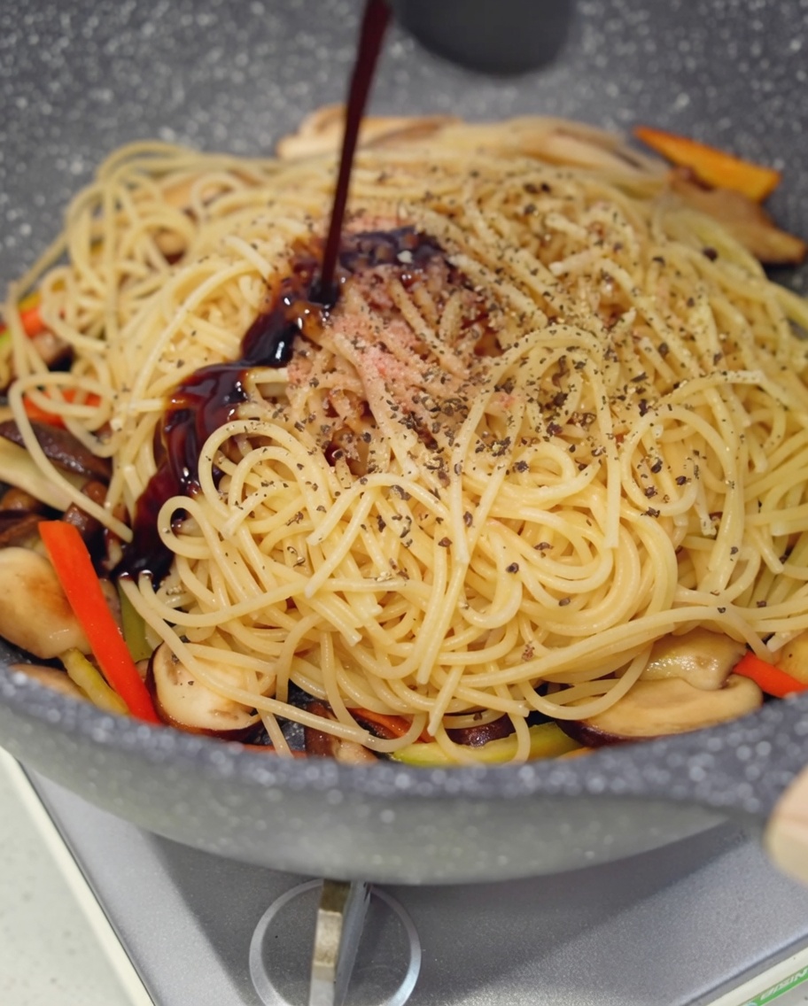 Sauce huître végane versée sur le mélange de pâtes.