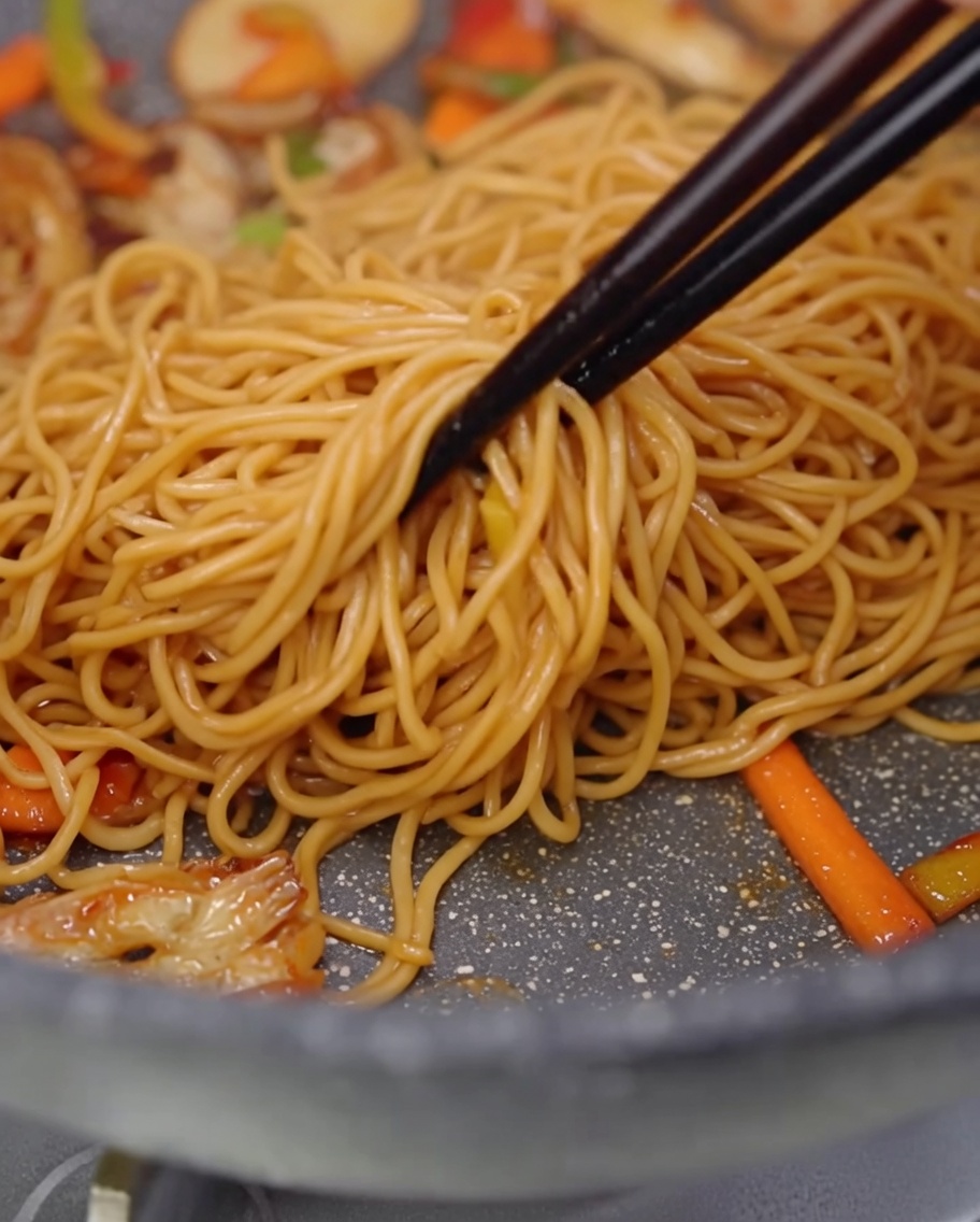 Gros plan sur les spaghetti, champignons et poivrons mélangés à laide de baguettes.