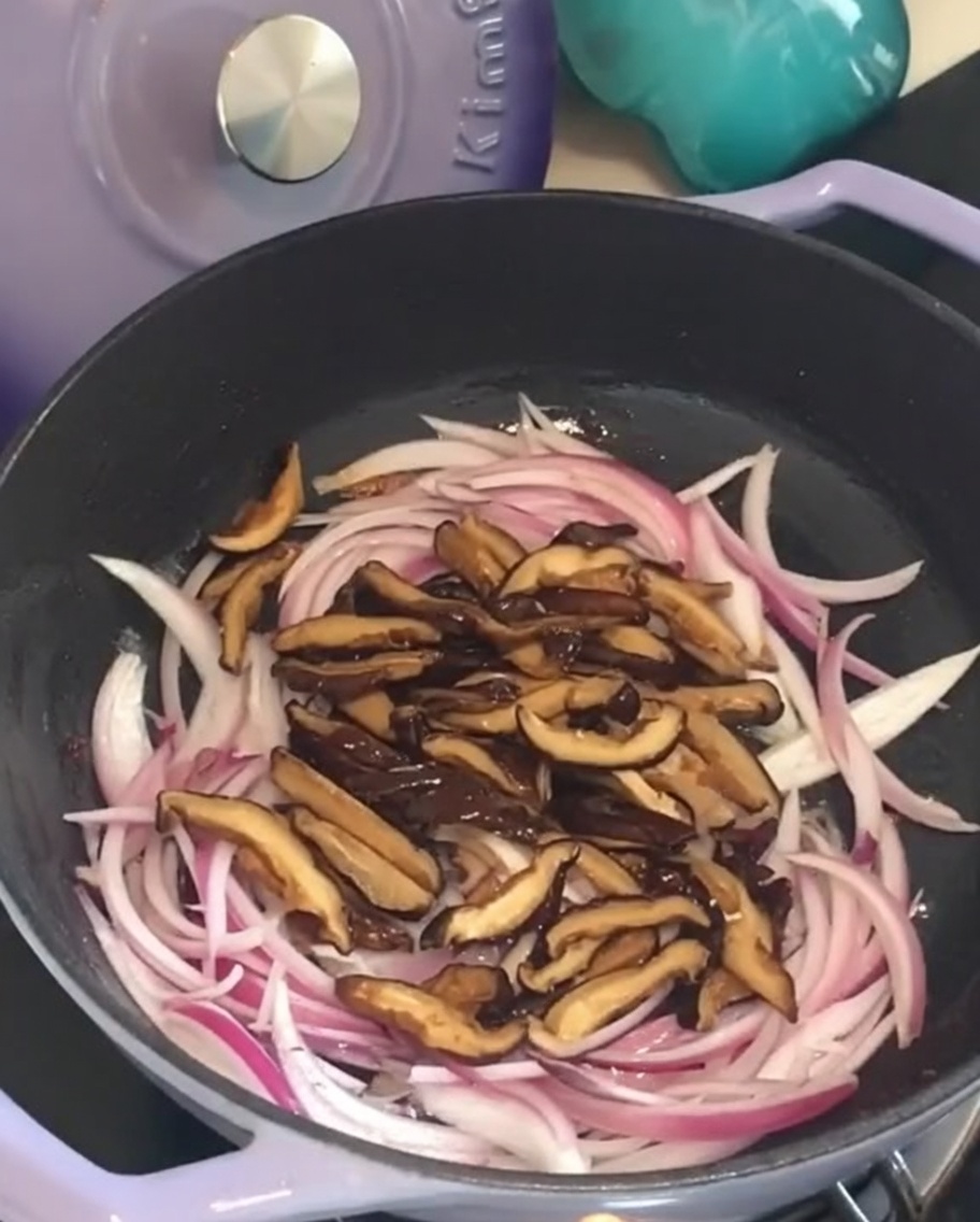 Champignons shiitake ajoutés sur les oignons dans la poêle.