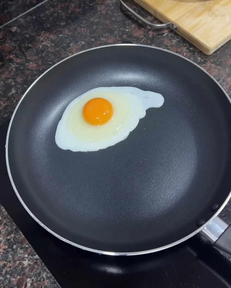 Un œuf frit dans une poêle noire avec du beurre fondu.