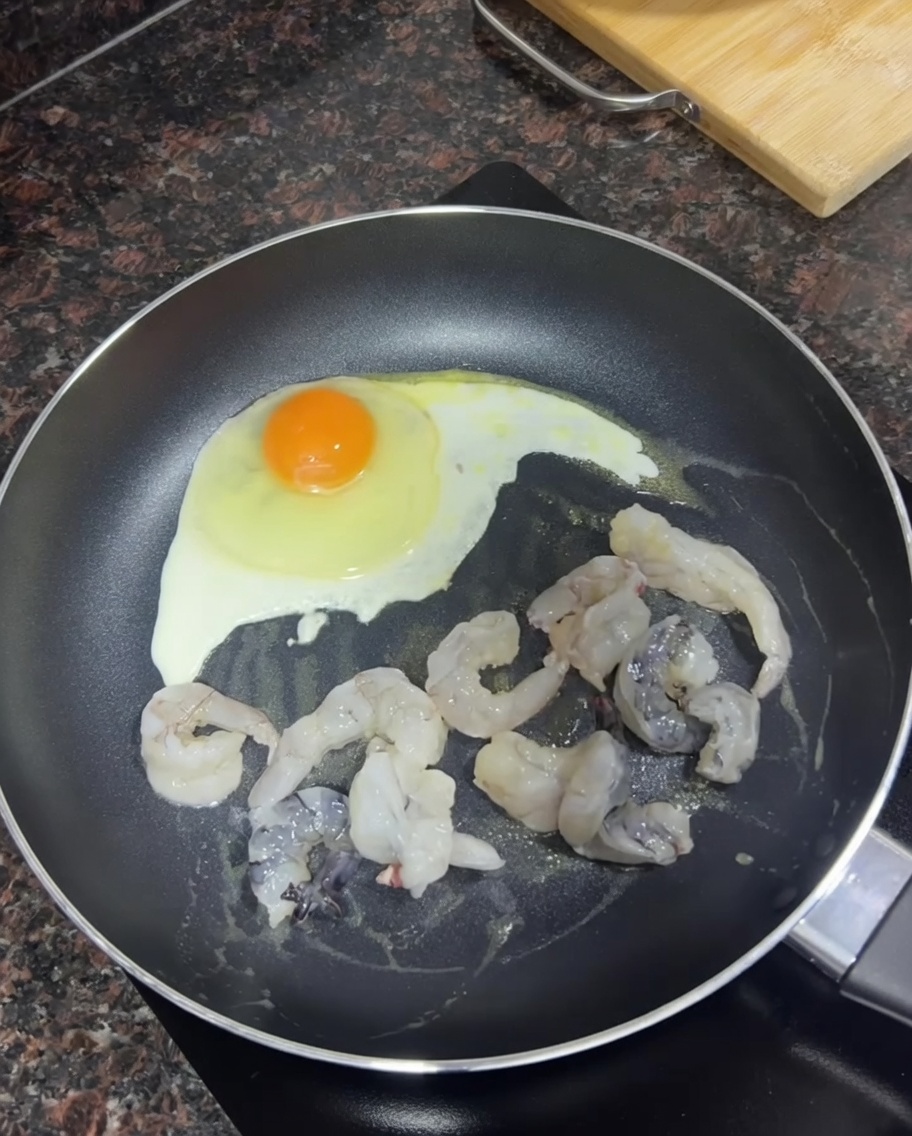 Crevettes crues brunissant dans une poêle à côté dun œuf frit.