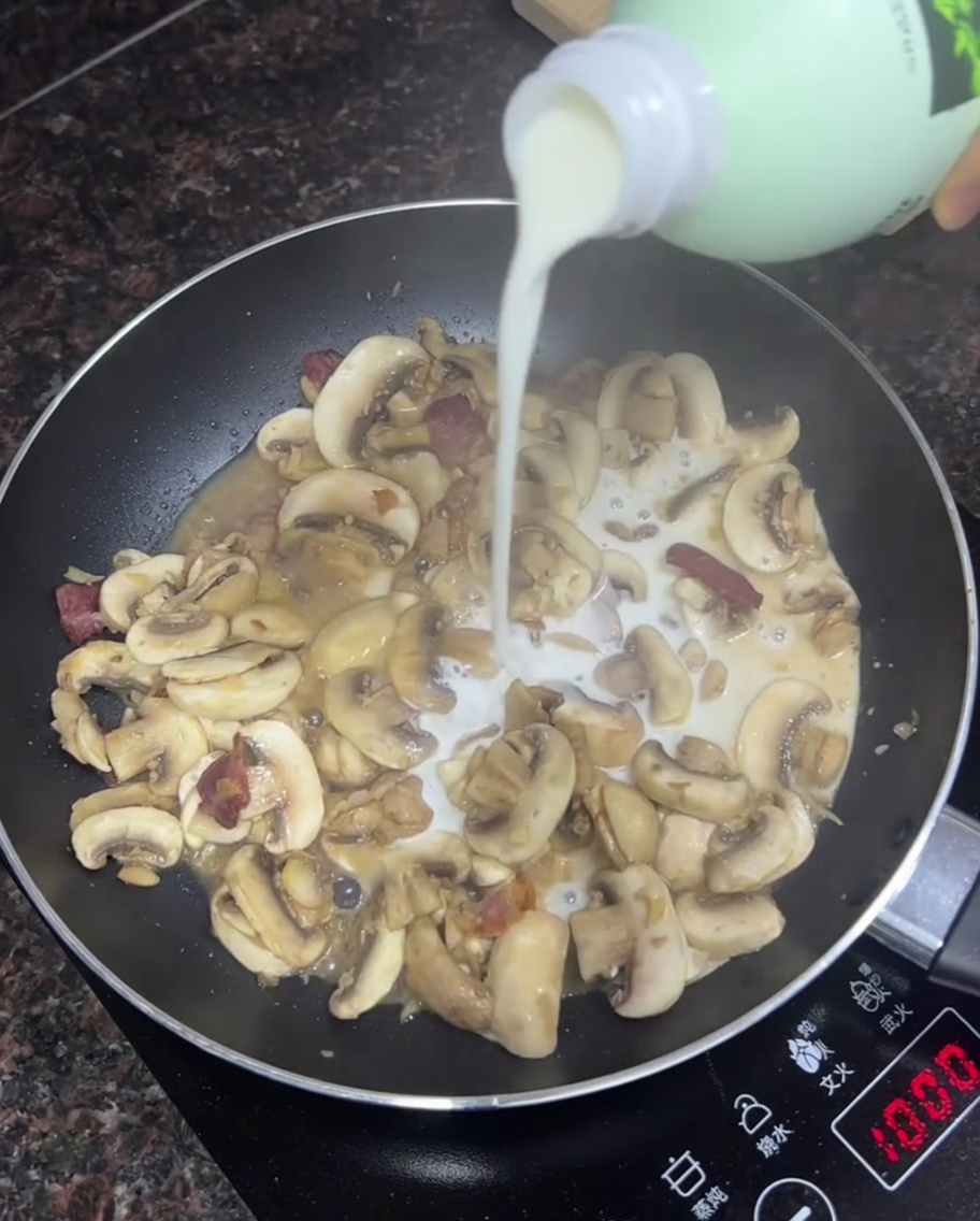 Lait versé dans une poêle avec des champignons et du bacon sautés.
