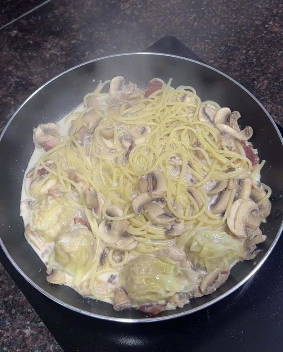 Poêle remplie de spaghettis crémeux, champignons émincés et quelques wontons cuits mijotant ensemble.