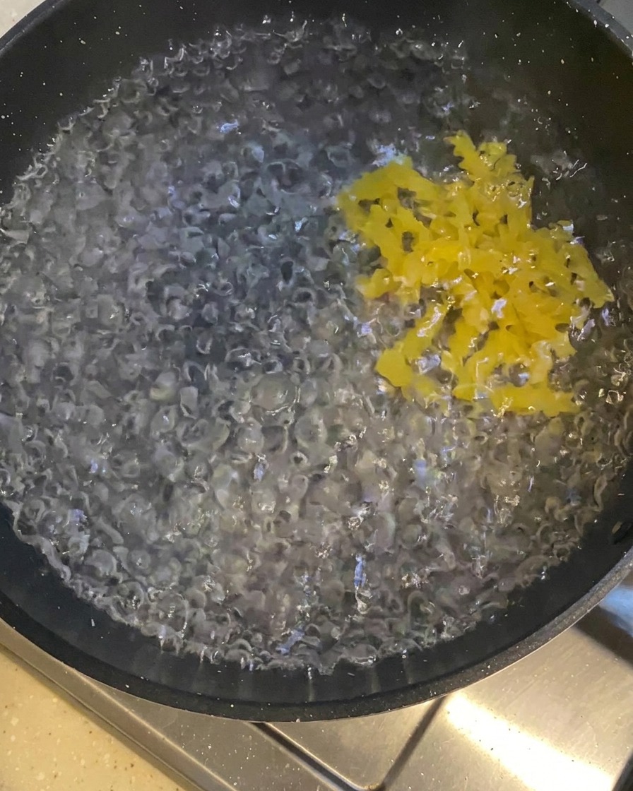 Pâtes torsadées jaunes versées dans une casserole deau bouillante bouillonnante.