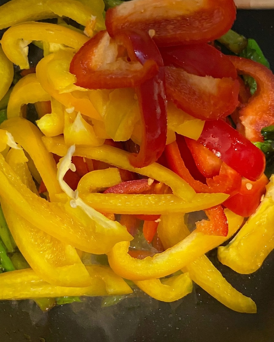 Lanières de poivrons jaunes et rouges ajoutées dans la poêle avec les asperges.