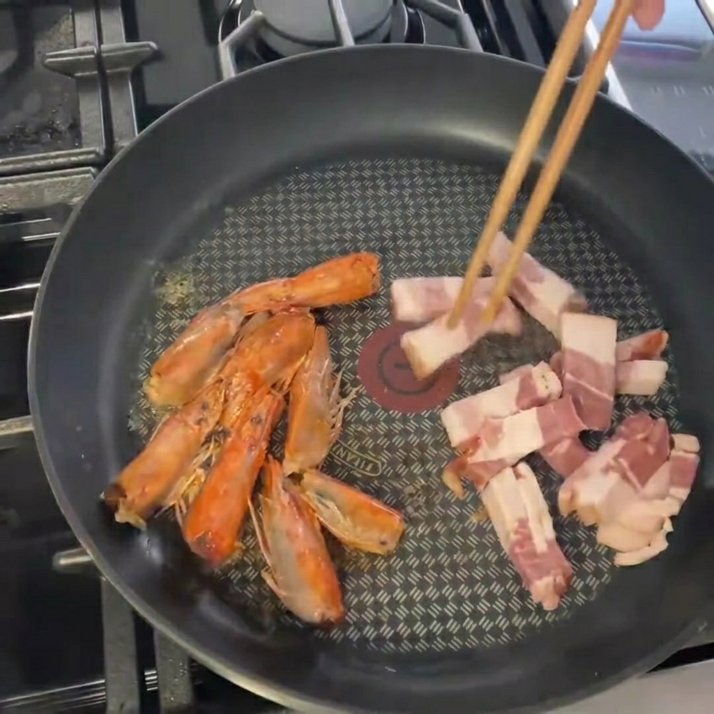 Morceaux de lard ajoutés à la poêle avec les têtes de crevettes.