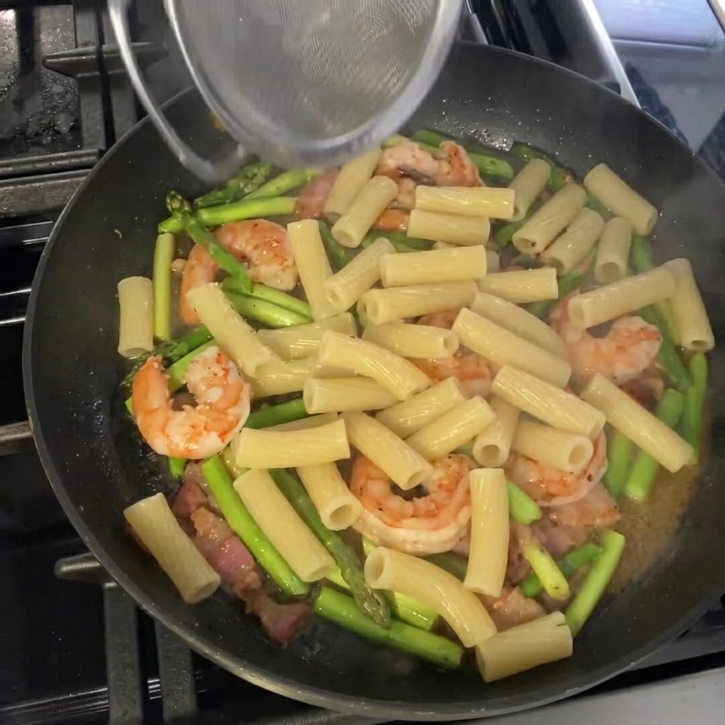 Rigatoni mélangés avec la sauce aux crevettes et asperges dans la poêle.