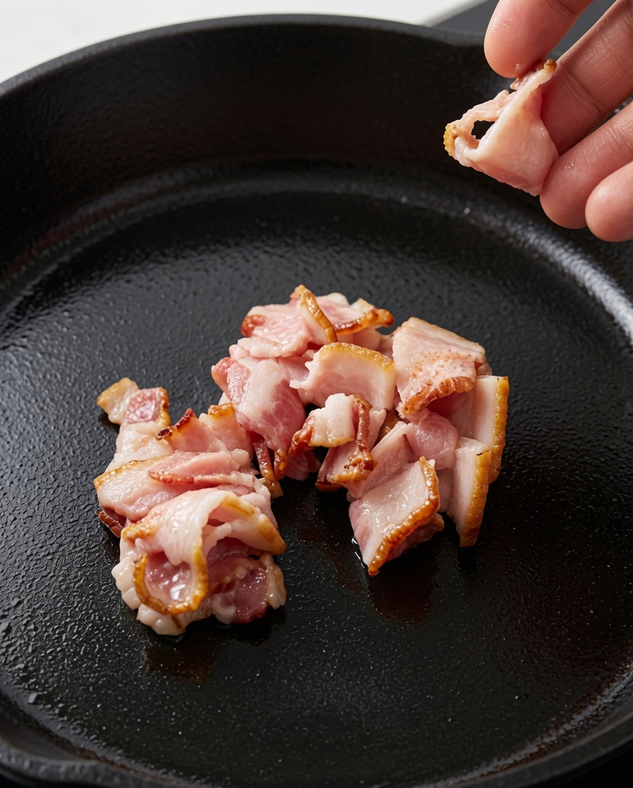 Une main dépose des morceaux de bacon cru dans une poêle en fonte sombre.