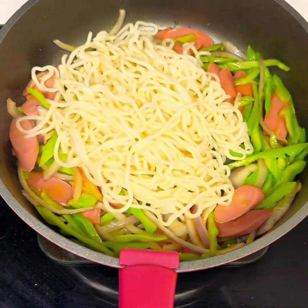 Nouilles et légumes dans une poêle, arrosés de sauce.