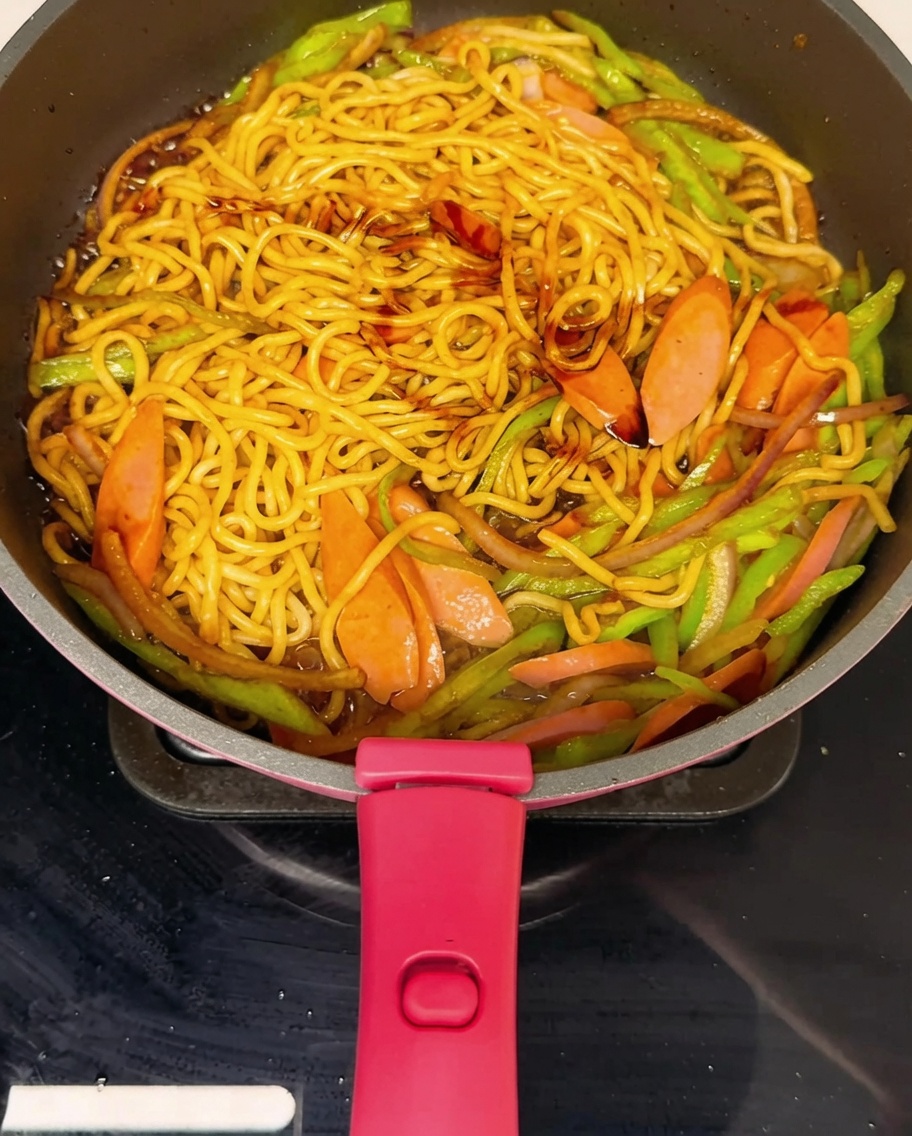 Nouilles sautées dans une poêle, saupoudrées de poivre noir fraîchement moulu.