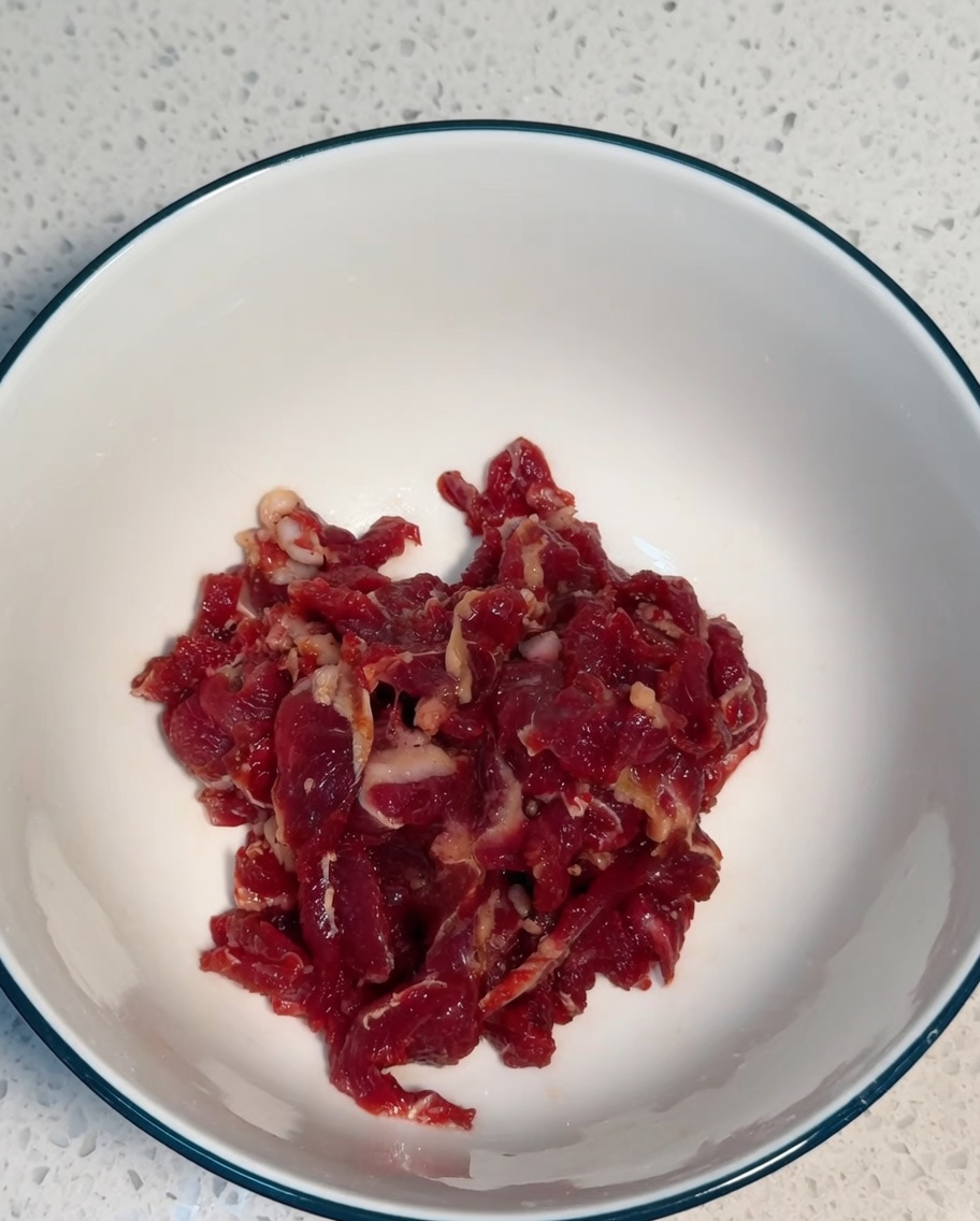 Bœuf finement émincé mélangé aux ingrédients de la marinade dans un bol blanc.