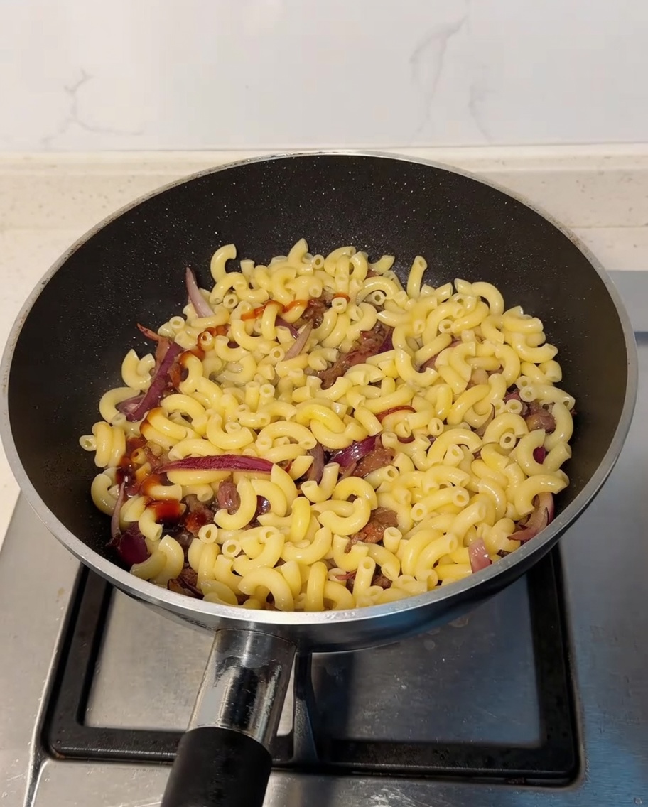 Sauce huître et sauce soja claire versées en filet sur le mélange de macaronis et de bœuf dans la poêle.