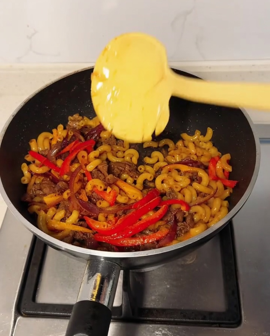 Une tranche de fromage sur le mélange de macaronis dans un wok, avec de la poudre de poivre noir saupoudrée par-dessus.