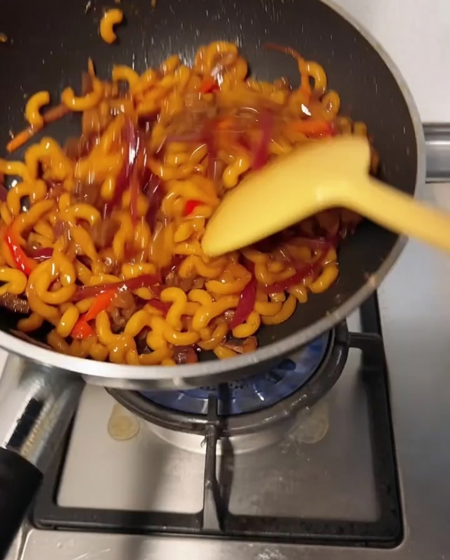 Mélange de macaronis remué dans le wok pendant que le fromage fond et enrobe les ingrédients.