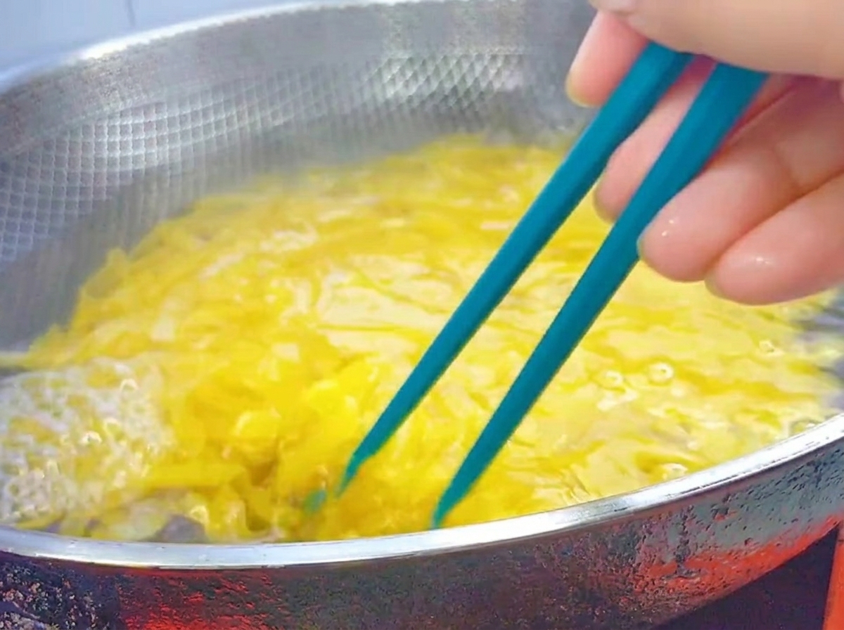Des baguettes bleues remuant des pennes en train de cuire dans un grand wok en acier inoxydable.