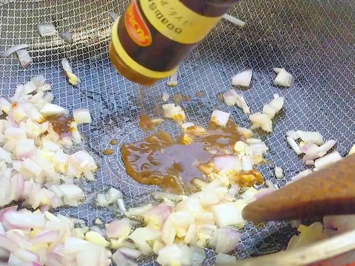 De la sauce au poivre noir versée depuis une bouteille dans un wok sur les aromates.