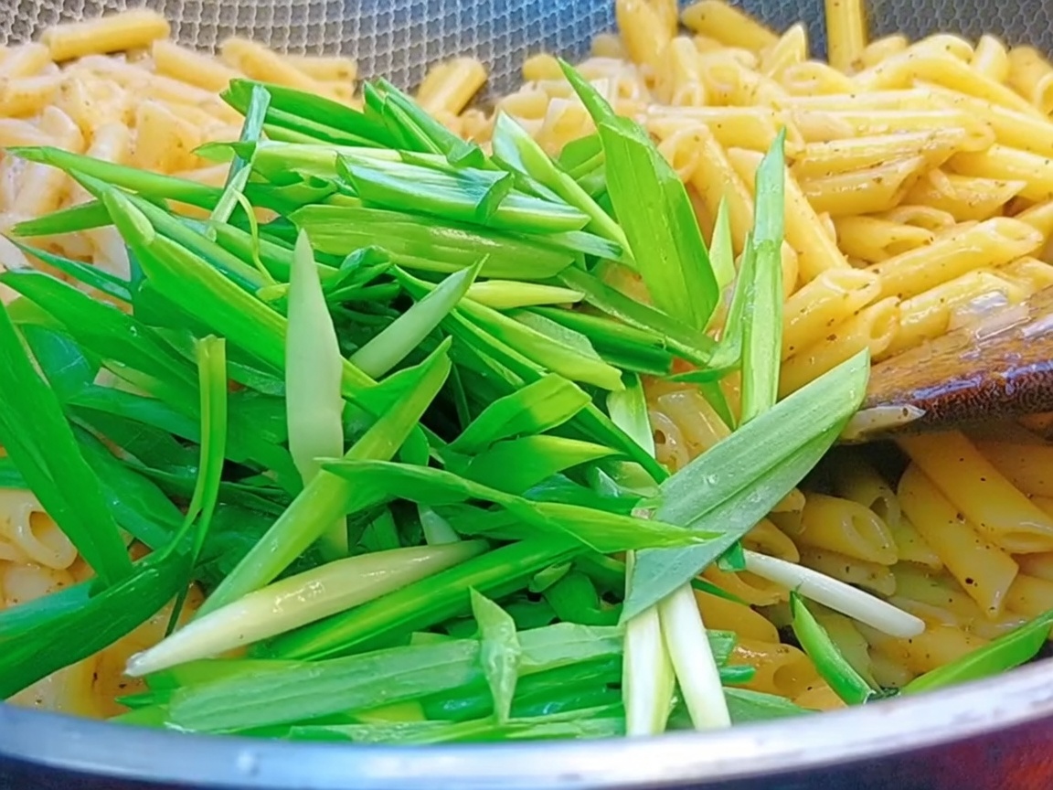 Des pousses dail fraîches jetées dans un wok rempli de pennes et de sauce au poivre noir.