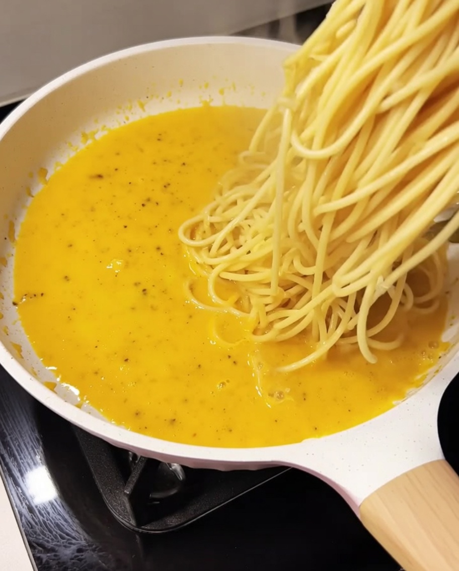 Spaghetti cuits ajoutés à la sauce crémeuse dans la poêle.