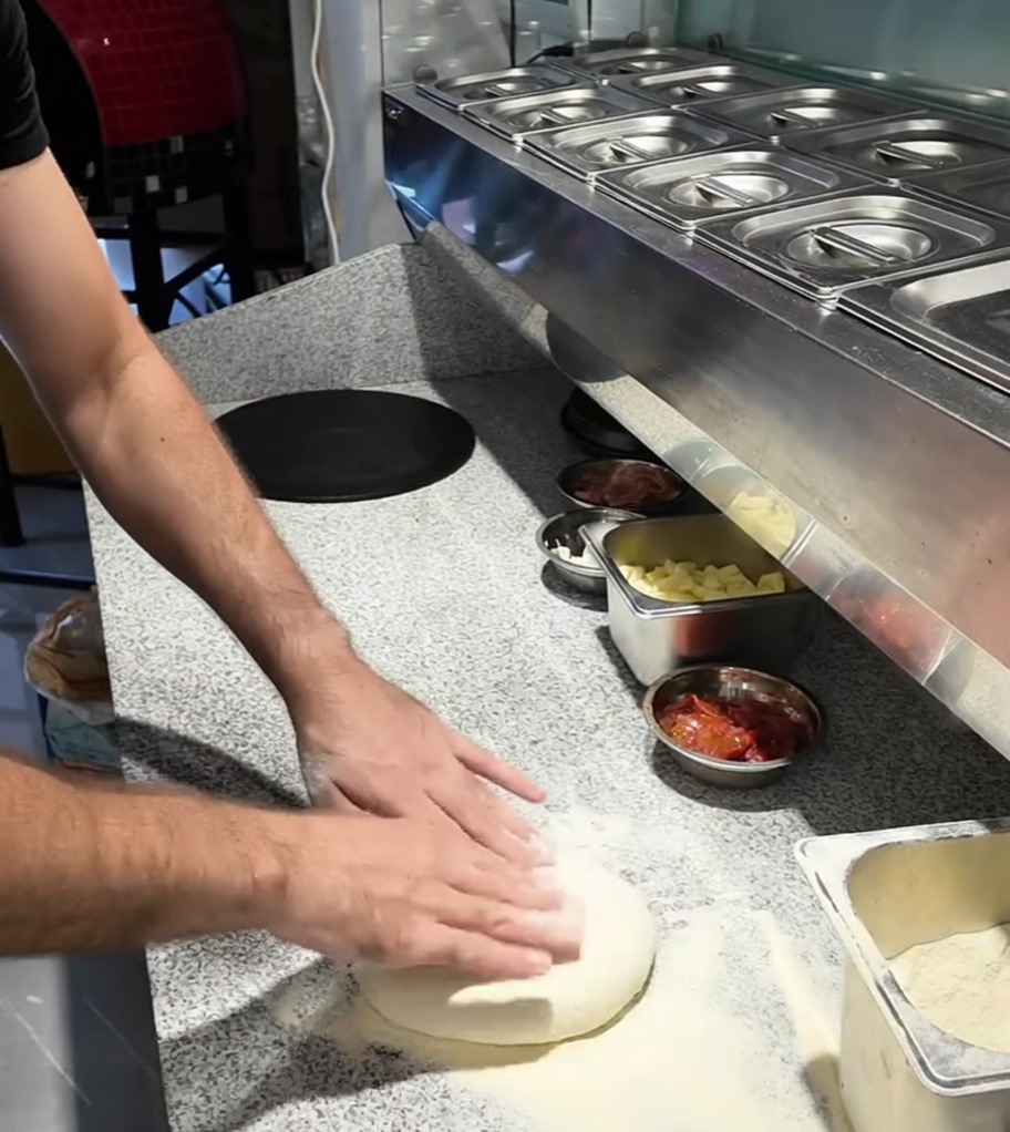 Mains étalant une boule de pâte à pizza sur un plan de travail fariné.