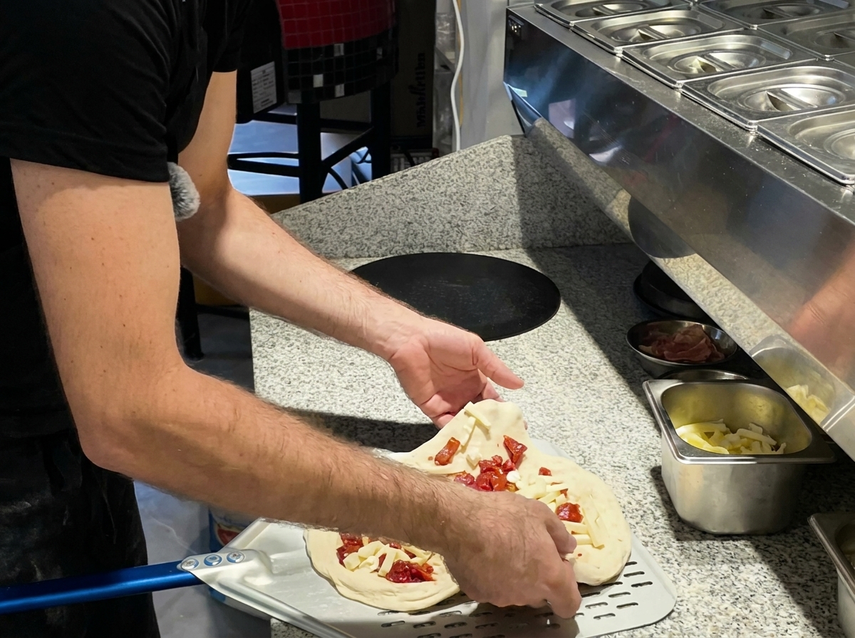Pizza glissée dans un four sur une pelle en métal.