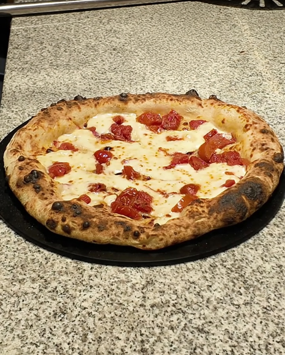 Pizza terminée sur un plan sombre garnie de tranches de pancetta.