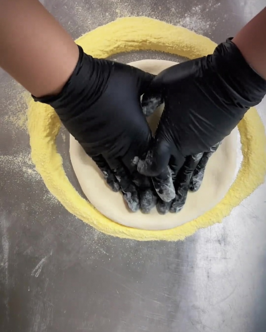 Mains gantées pressant le centre de la pâte à pizza pour laplanir uniformément.