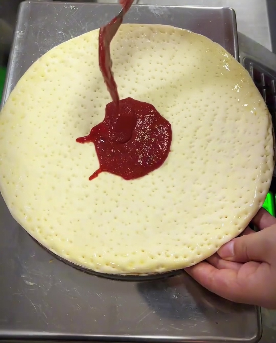 Sauce tomate étalée sur la pâte à laide du dos dune cuillère en métal.