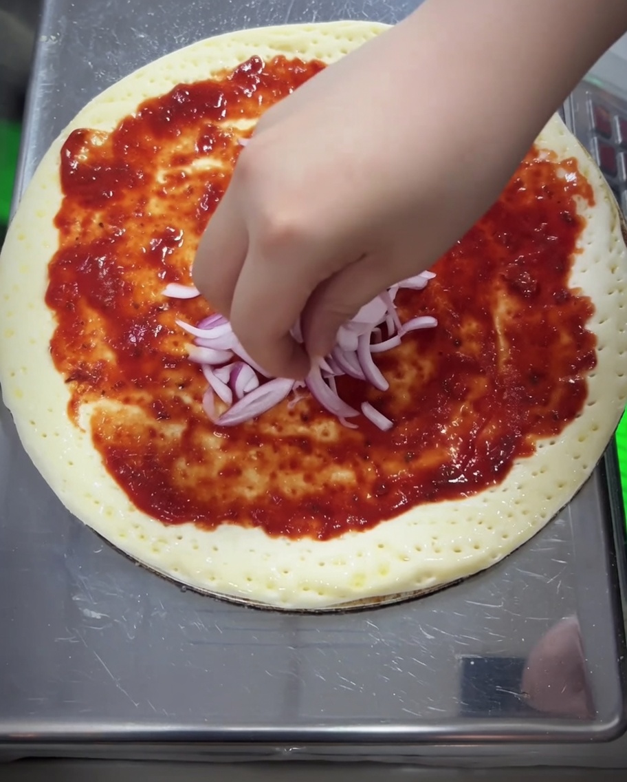 Morceaux doignon rouge et couche épaisse de mozzarella râpée ajoutés sur la pizza.