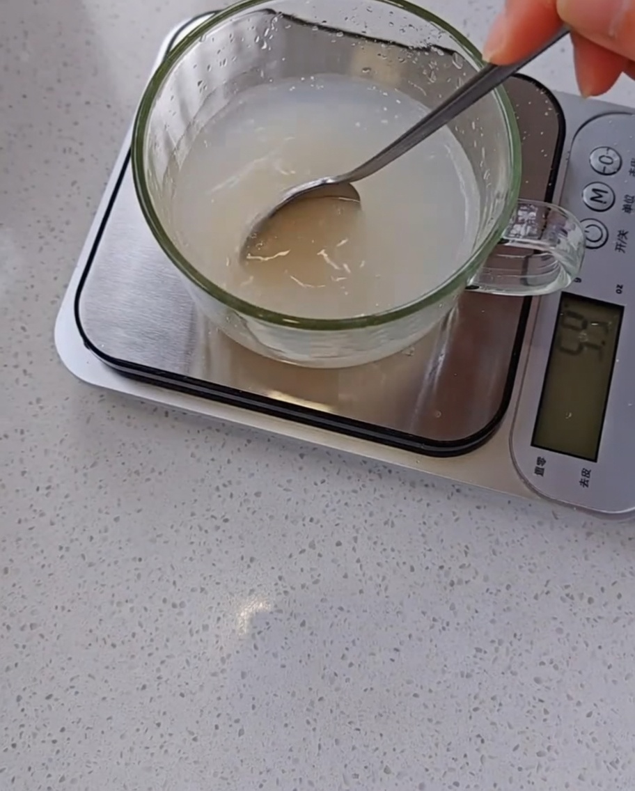 Une main utilisant une cuillère pour mélanger de la levure et de leau dans un verre doseur.
