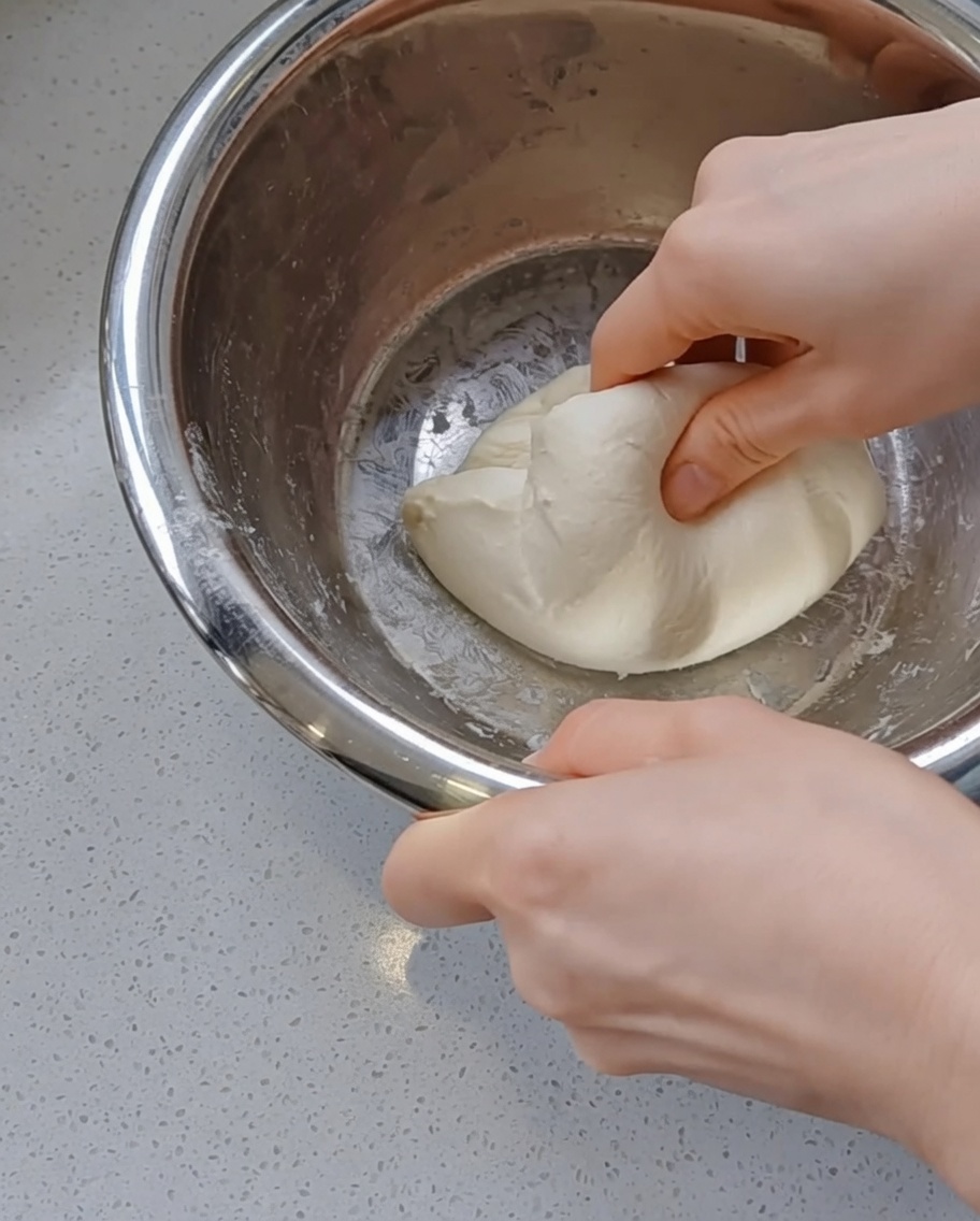 Mains façonnant une boule de pâte lisse.