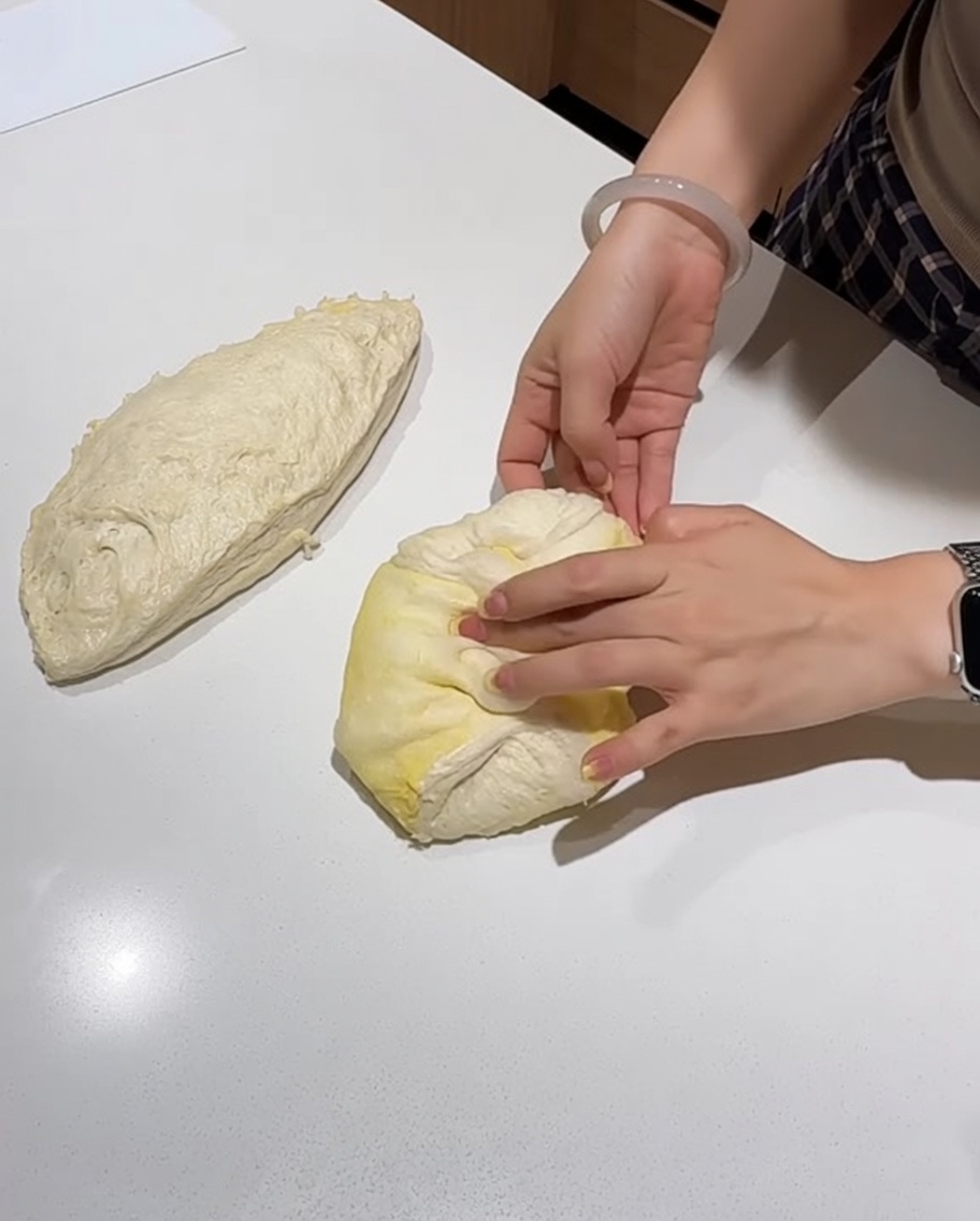 Les mains pliant et façonnant une portion de pâte à pizza en une boule lisse sur le comptoir.