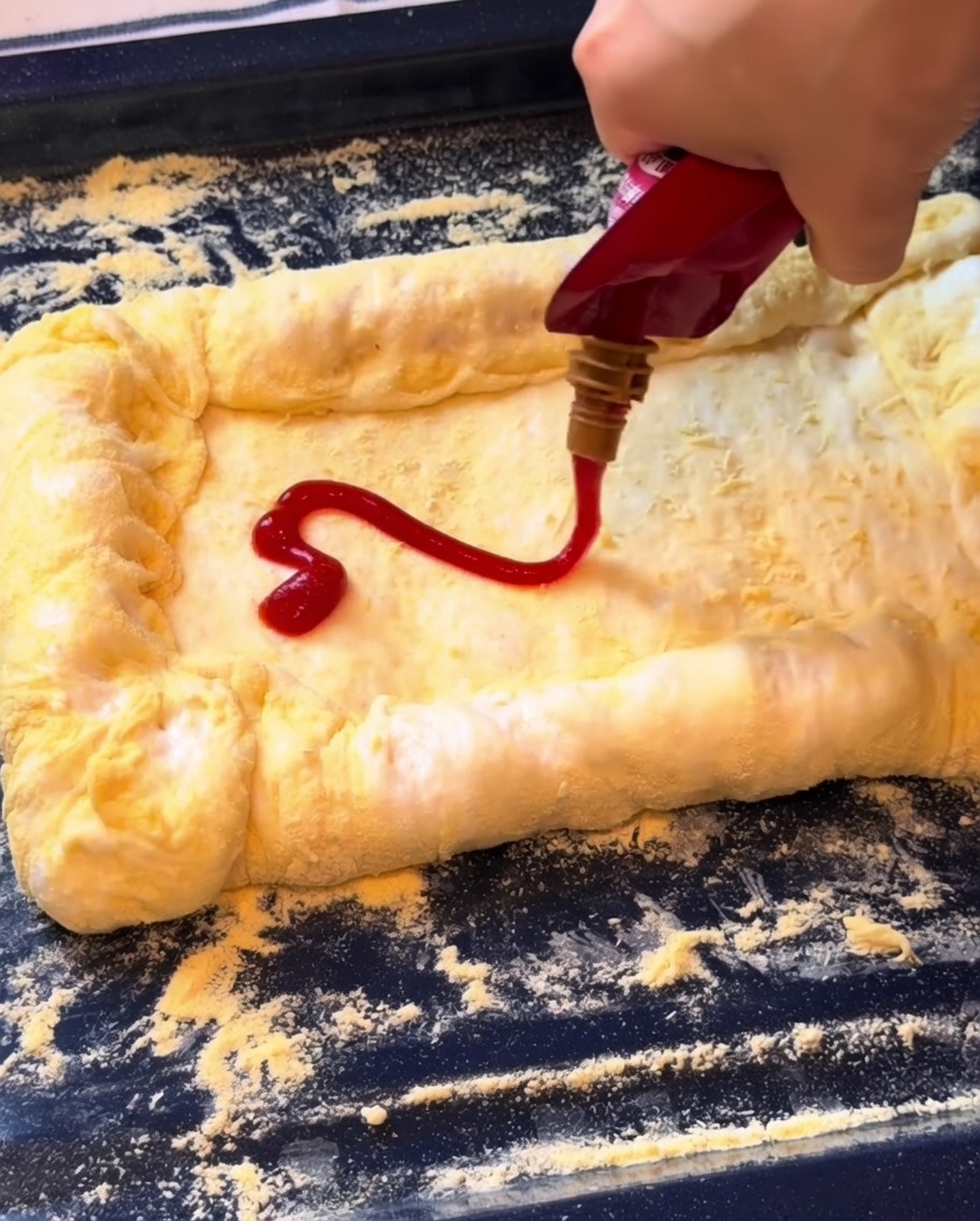 Ketchup étalé sur la base de la pizza, suivi dune couche de mozzarella râpée.