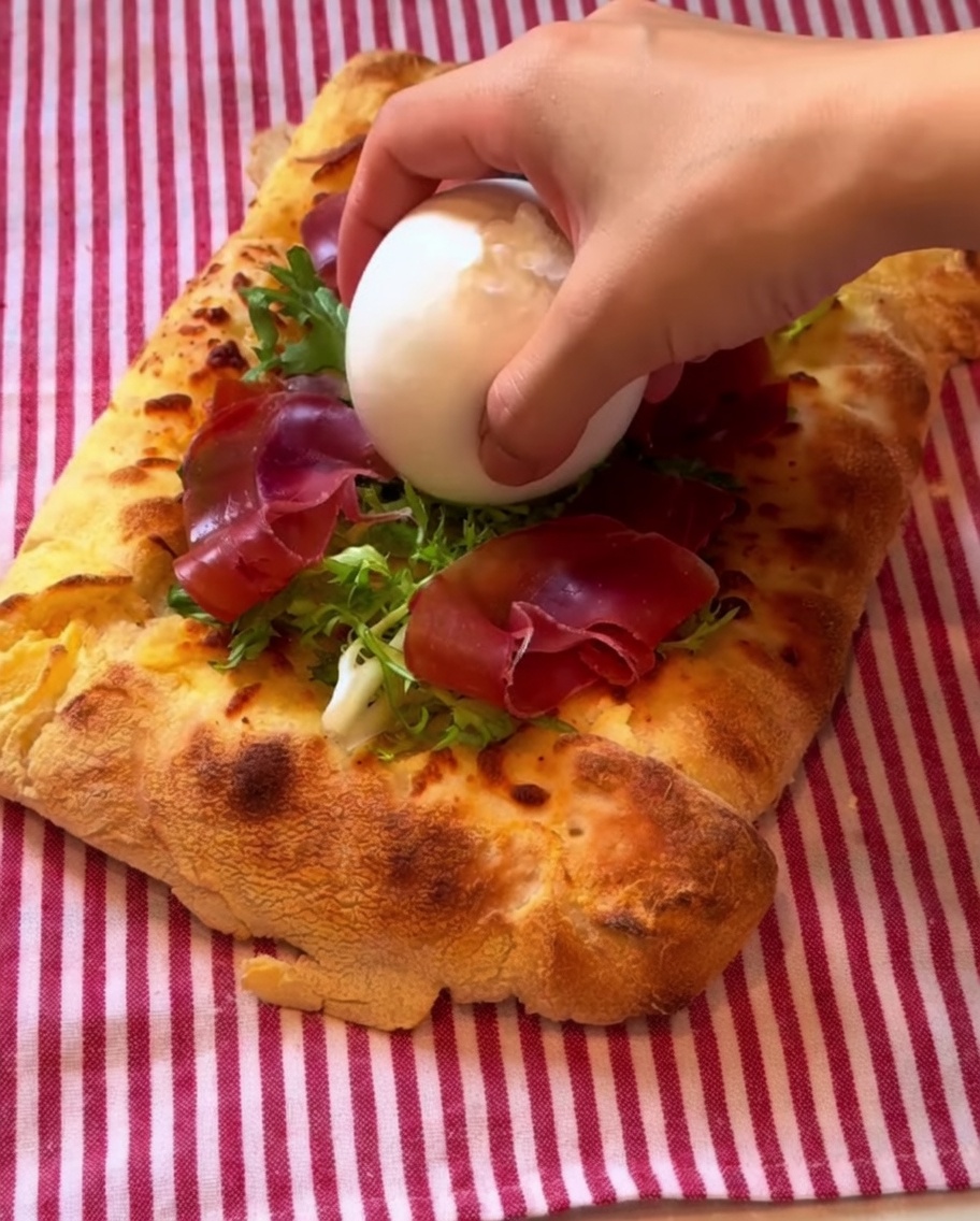 Une boule de burrata déposée sur la pizza, arrosée de vinaigrette balsamique.